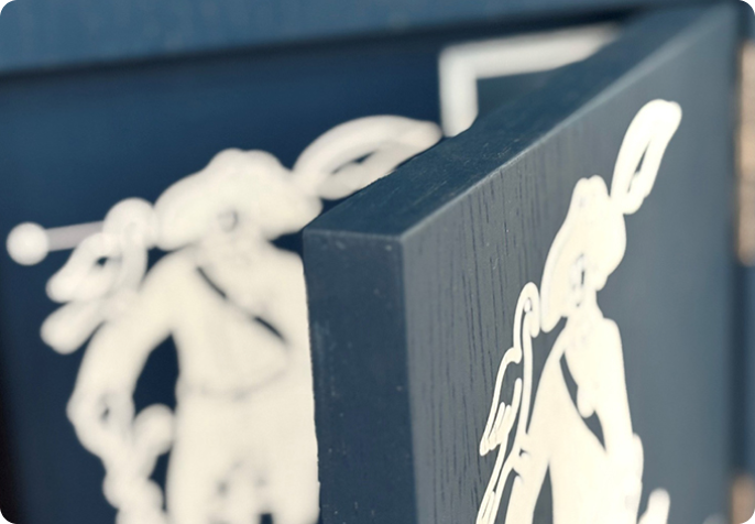 image_3_mobilier Détail d’une structure en bois bleu ornée d’un motif blanc représentant un personnage stylisé.