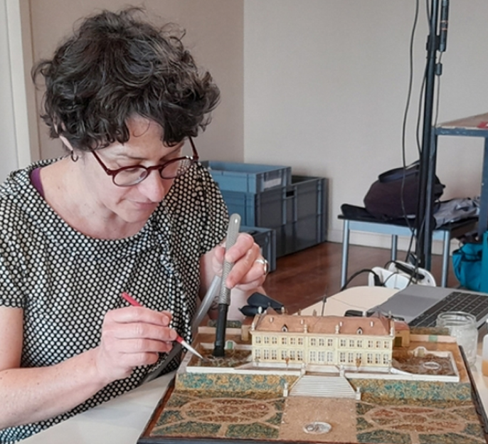 Femme concentrée sur la restauration d’une maquette de bâtiment historique.